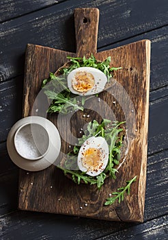 Sandwich with arugula, boiled egg and mustard on a wooden board.