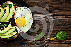 Sandwich with avocado, spinach and fried egg in a pan. Dark  wooden background and place for an inscription