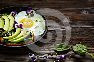 Sandwich with avocado, spinach and fried egg in a pan. Dark  wooden background and place for an inscription