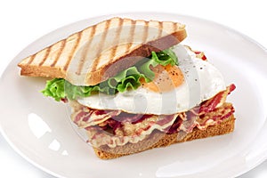 Sandwich with bacon, fried egg and lettuce on a plate.