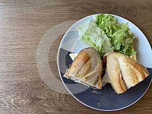 Sandwich baguette bacon and fried egg with salad on black white plate on wooden table