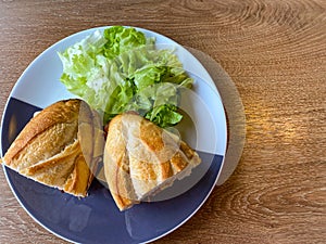 Sandwich baguette bacon and fried egg with salad on black white plate on wooden table