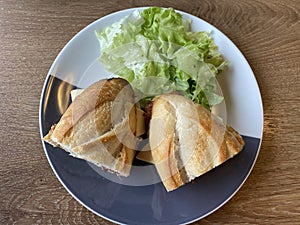 Sandwich baguette bacon and fried egg with salad on black white plate on wooden table