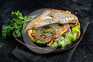 Sandwich balik Ekmek with grilled fillet of mackerel fish, tomatoes, onions and lettuce. Black background. Top view