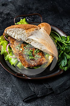 Sandwich balik Ekmek with grilled fillet of mackerel fish, tomatoes, onions and lettuce. Black background. Top view