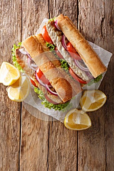 Sandwich balik Ekmek with grilled fillet of mackerel, tomatoes, onions and lettuce served with lemon closeup on the table.