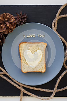 sandwich for breakfast in form of heart with cheese on a blue plate and black background with cones inscription I love you