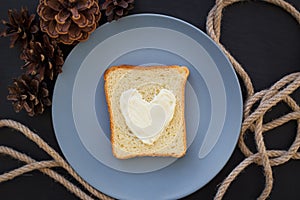 Sandwich for breakfast in form of heart with cheese on a blue plate and black background with cones