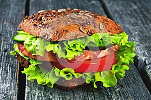Sandwich with cereals bread, with ham and vegetables, green salad on wooden background