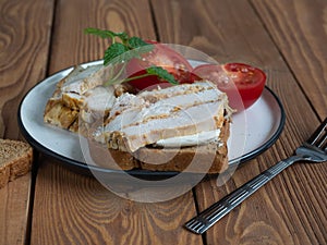 Sandwich with chicken ham and sliced tomato on a ceramic plate on a wooden table