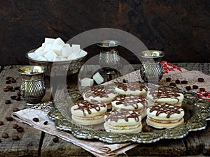 Sandwich cookies with cream decorated with chocolate on a metal platter and sprinkle with coffee beans around.