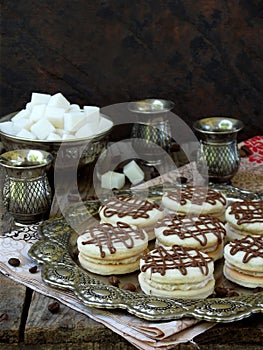 Sandwich cookies with cream decorated with chocolate on a metal platter and sprinkle with coffee beans around.