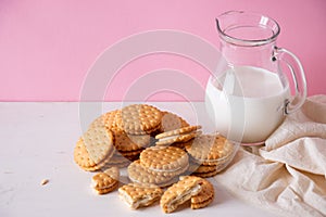 Sandwich cookies and a glass of milk on a pink background. The concept of breakfast and a quick snack