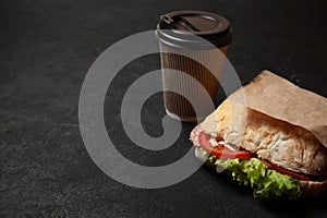 Sandwich and cup of coffee on black background. Morning breakfast or snack when hungry. Street food to go. Copy space for text.