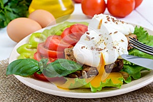 Sandwich with egg poached, lettuce, black bread with seeds, tomatoes, sweet pepper on a plate