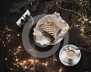Sandwich and espresso surrounded by New Year`s lights and pine branches. Food dark background. Christmas lunch in a cafe