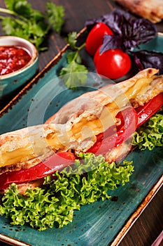 Sandwich with fillet grilled chicken, lettuce, tomatoes, cheese and traditional bread loaf out of the oven on dark background.