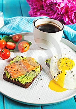 Sandwich with fried egg, avocado and salted salmon with a cup of aromatic coffee for breakfast