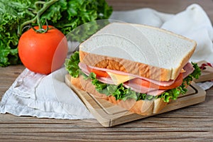 Sandwich with ham, cheese and vegetables on wood table