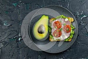Sandwich with ham and tomatoes on gray plate with avocado