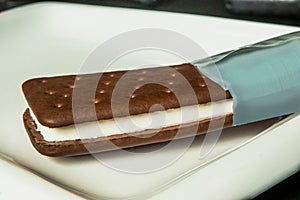 sandwich. ice cream. sweet chocolate and ice cream sandwich dessert with a wrapping in a white plate on black ground.
