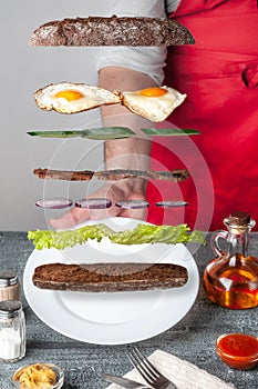 Sandwich ingredients are levitated in the air with crispy baguette, lettuce, cucumber, red onion, grill meat and scrambled eggs.