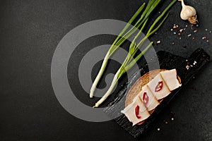 sandwich with lard and red pepper on a black cutting board on a black background