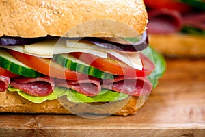 Sandwich with lettuce, slices of fresh tomatoes, cucumber, red onion, salami and cheese