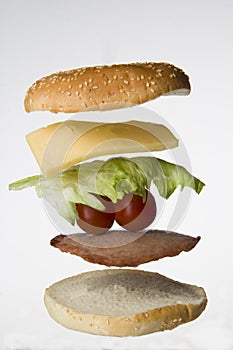 Sandwich made of white buns, meat, tomatoes, cheese, salad arranged horizontally and isolated on a white background