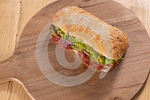 Sandwich with meat, salad, and cheese on a wooden board. Chabata