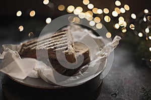 Sandwich on a plate surrounded by New Year`s lights and pine. Food on a dark background. Christmas mood in a cafe