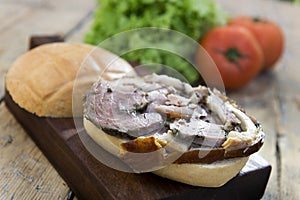 Sandwich with porchetta on cutting board with salad and tomatoes