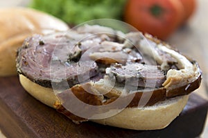 Sandwich with porchetta on cutting board with salad and tomatoes