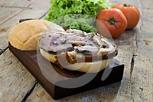 Sandwich with porchetta on cutting board with salad and tomatoes