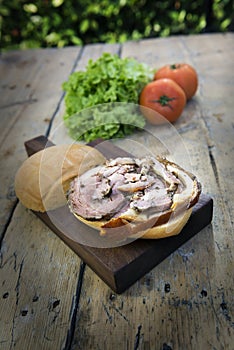 Sandwich with porchetta on cutting board with salad and tomatoes