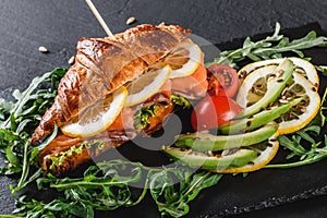 Sandwich with red fish, avocado, fresh vegetables and arugula on black shale board over black stone background. Healthy food