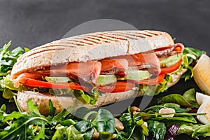 Sandwich with red fish, eggs, avocado, fresh vegetables and greens on black shale board over black stone background