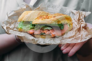 Sandwich with salmon on kraft paper in the hands of a woman