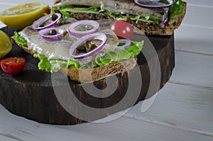 Sandwich with salted herring, butter and red onion on old rustic cutting board. Selective focus