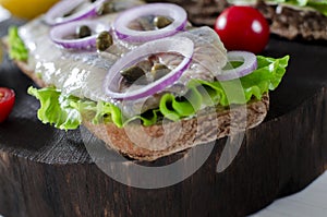Sandwich with salted herring, butter and red onion on old rustic cutting board. Selective focus