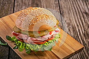 sandwich with sausage, cucumber, tomato and lettuce leaves on wooden background