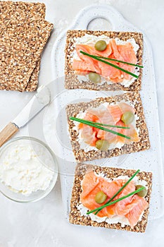 Sandwich with smoked salmon and cream cheese on thin multi seed  crispbread, garnished with green onion and olives, vertical,  top