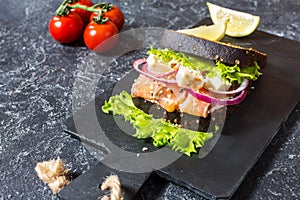 Sandwich with smoked salmon, tomato, onions and salad on stone background