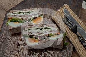 Sandwich stuffed with chicken breast, cheese, boiled eggs and fresh vegetables serve with fork and knife on wooden plate