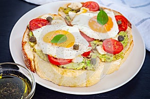 Sandwich toasts with agg, tomatoes cherry, mozzarella, avocado, basil and olive oil. Side view on a dark stone