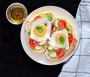 Sandwich toasts with agg, tomatoes cherry, mozzarella, avocado, basil and olive oil. Top view on a dark stone background