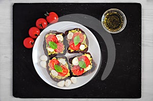 Sandwich toasts with tomatoes cherry, mozzarella, avocado, basil and olive oil. Top view on a dark stone dish. Flat lay.