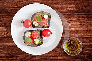 Sandwich toasts with tomatoes cherry, mozzarella, avocado, basil and olive oil. Top view on a dark wooden background