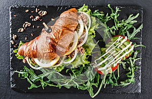 Sandwich with tuna, avocado, fresh arugula and greens on black shale board over black stone background