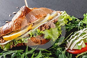 Sandwich with tuna, avocado, fresh arugula and greens on black shale board over black stone background. Healthy food